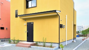 A modern yellow building with a black door and window, surrounded by gravel and small plants. - Alloggio Nanki Shirahama (Shirahama)