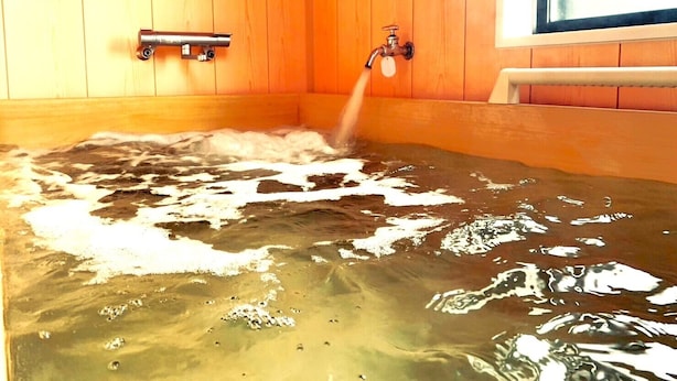 A wooden-paneled room with a bathtub filled with water and a faucet. - Alloggio Nanki Shirahama (Shirahama)