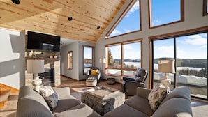 A spacious living room with a high ceiling, large windows, and a fireplace. - Lax Lake View Retreat (Silver Bay)