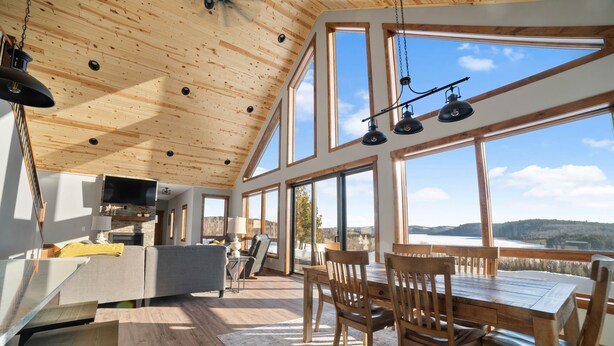 A spacious room with a high ceiling, large windows, a dining area with wooden furniture, and a view of the outdoors. - Lax Lake View Retreat (Silver Bay)