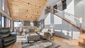 A spacious living area with a high ceiling, a staircase, and a kitchen in the background. - Lax Lake View Retreat (Silver Bay)