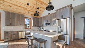 A modern kitchen with wooden cabinets, a central island with stools, stainless steel appliances, and a wooden ceiling. - Lax Lake View Retreat (Silver Bay)