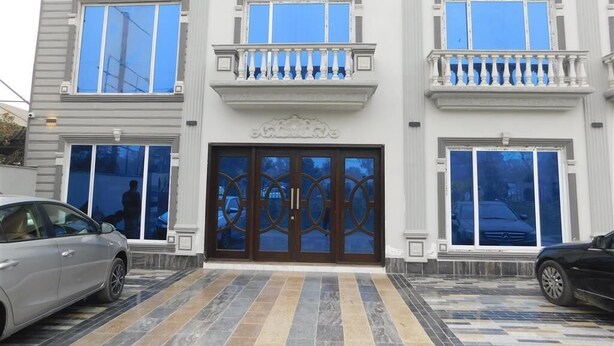 A multi-story building with a central entrance featuring a large, ornate door and a balcony with a balustrade. - Amada Hotel (Lahore)