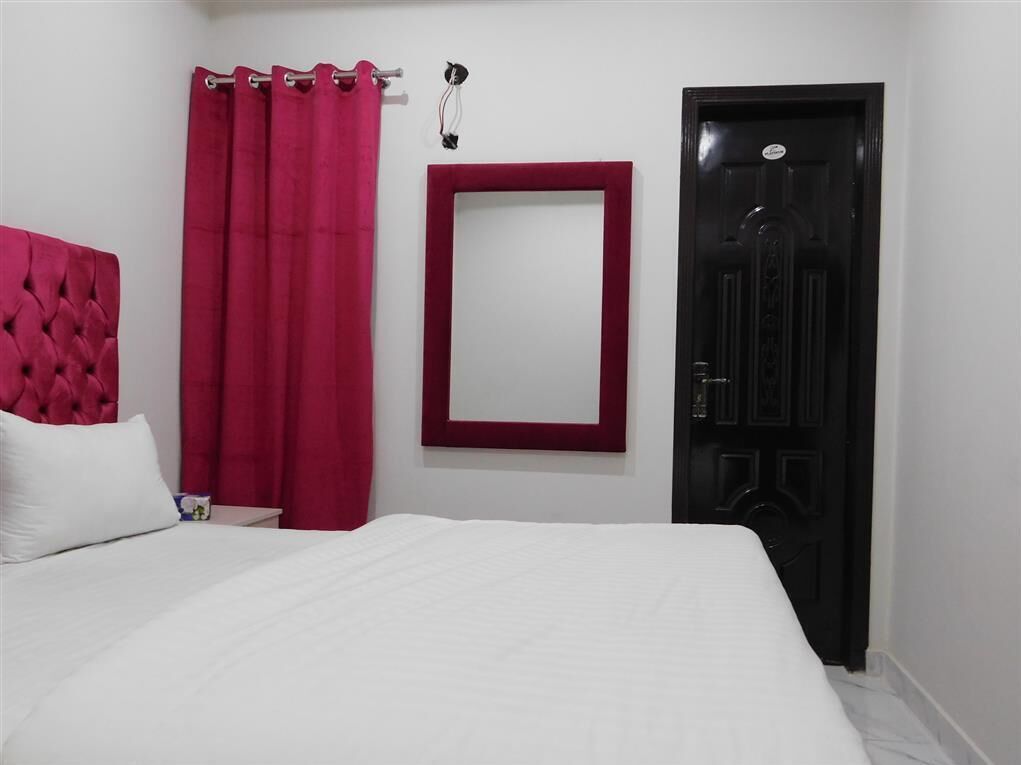 Ein Schlafzimmer mit einem großen Bett, einem roten Vorhang, einer schwarzen Tür und einer weißen Wand.