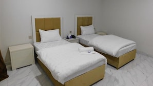 A hotel room with two single beds, a nightstand, and a small table with a lamp. - Amada Hotel (Lahore)