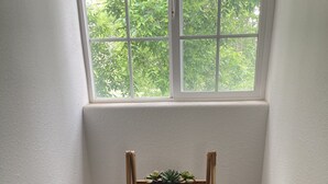Une petite salle de bain d’angle avec une étagère en bois où sont posées des serviettes et une petite plante.