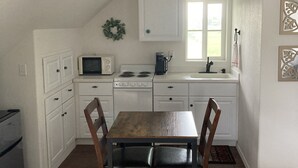 Une cuisine de taille réduite avec des meubles blancs, une table à manger en bois et un ventilateur de plafond.