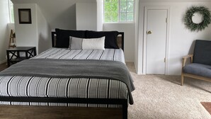 Une chambre à coucher avec un lit, une fenêtre, une porte, une chaise et une couronne décorative accrochée au mur.