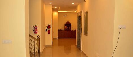 A hotel hallway with a polished floor, a fire extinguisher, a reception desk, and a wall-mounted light switch.