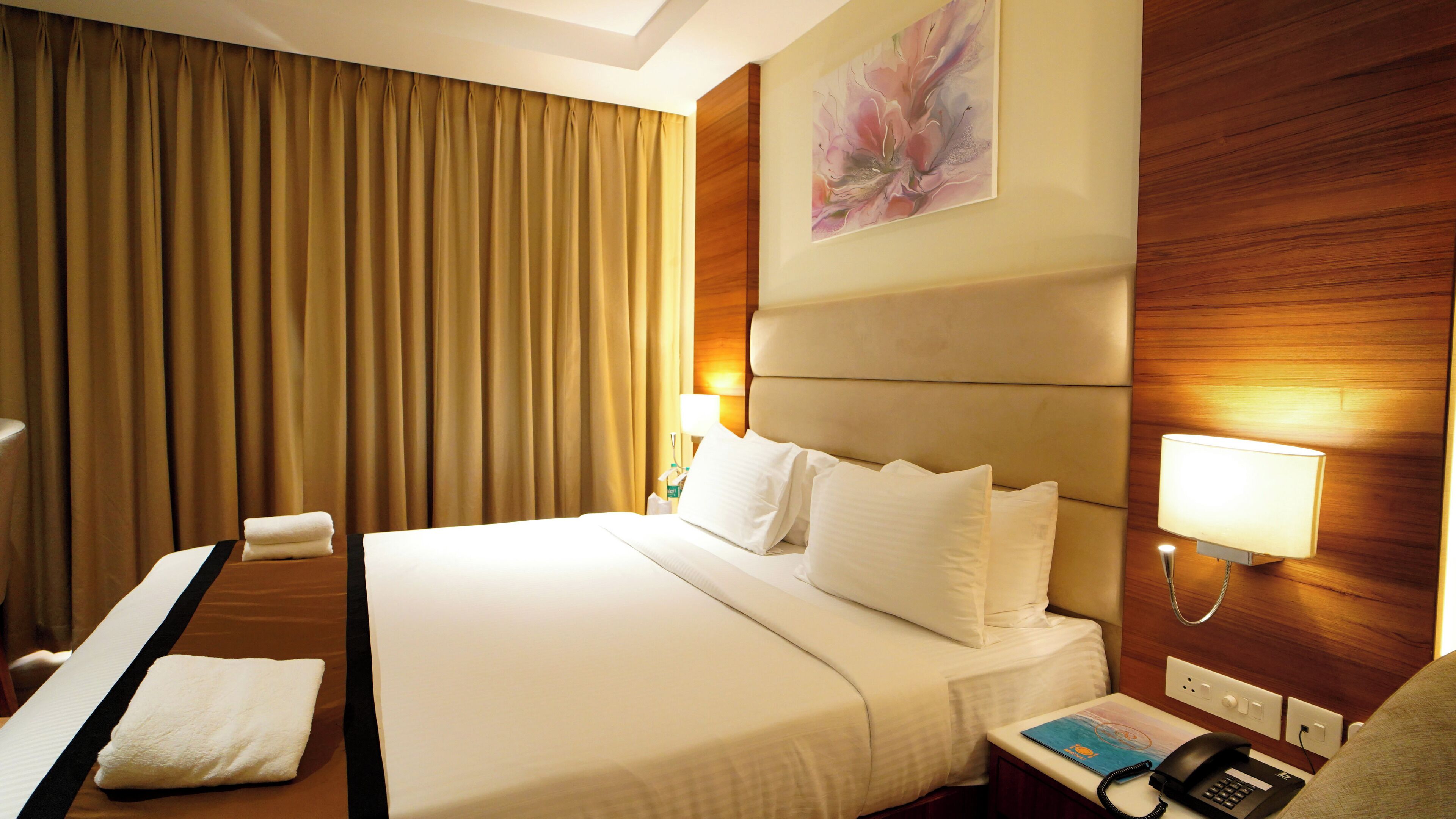 A hotel room with a large bed, a desk, a chair, a telephone, and a painting on the wall.