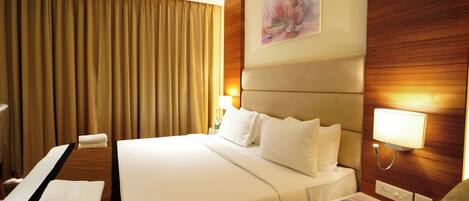 A hotel room with a large bed, a desk, a chair, a telephone, and a painting on the wall.