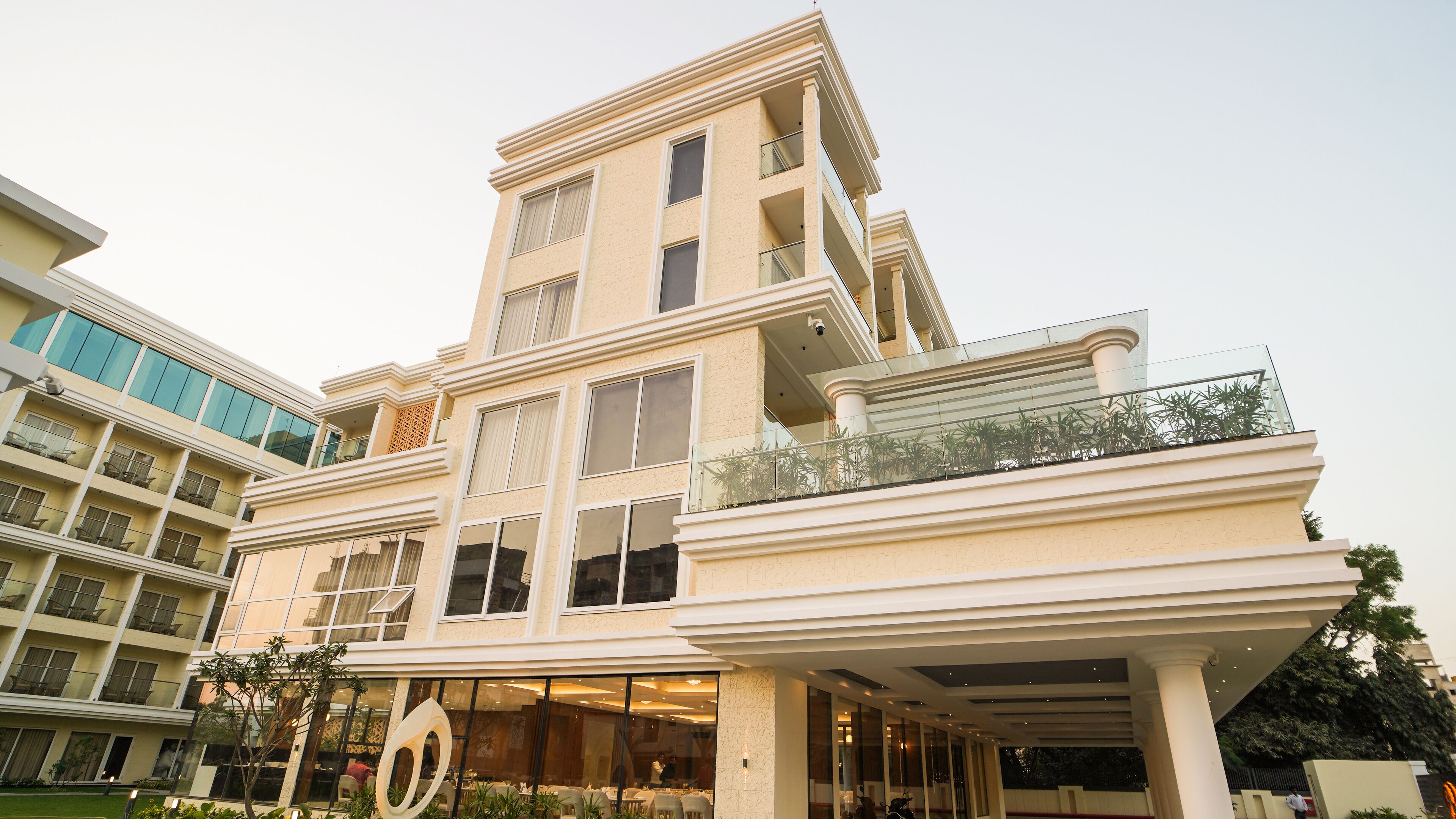 A multi-story hotel with a modern design, featuring balconies with glass railings and a central atrium with a dining area.