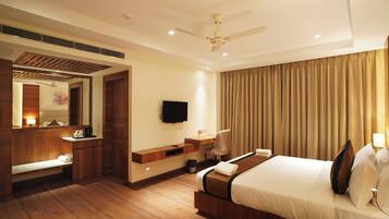 A hotel room with a bed, a desk, a TV, a mirror, and a ceiling fan.