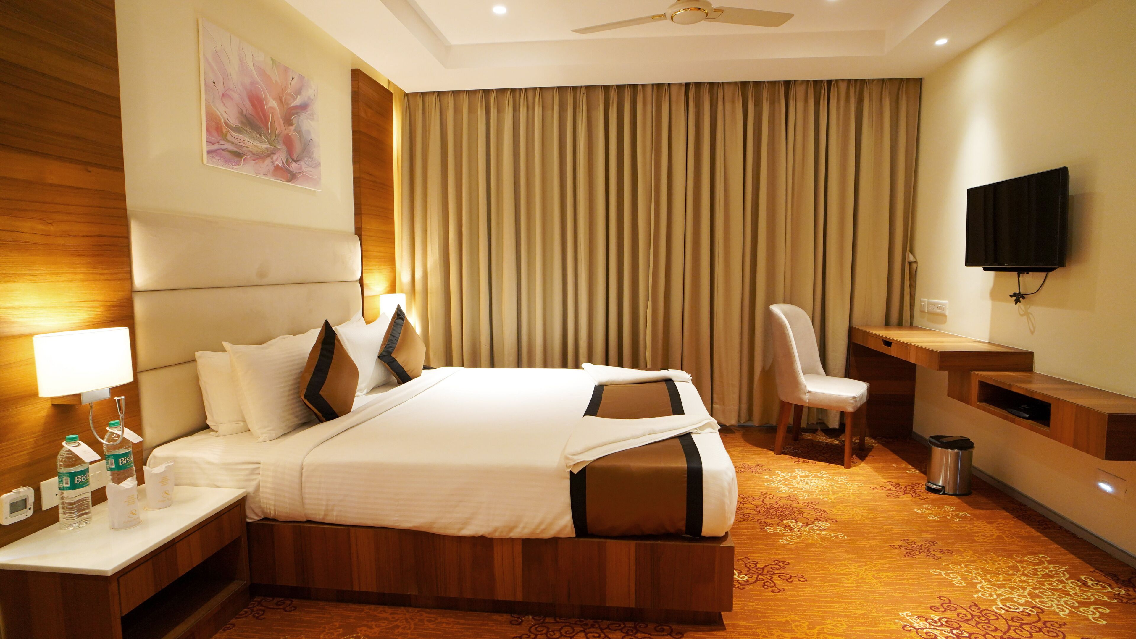 Habitación de hotel con una cama grande, un escritorio con silla, televisión y televisor de pared.