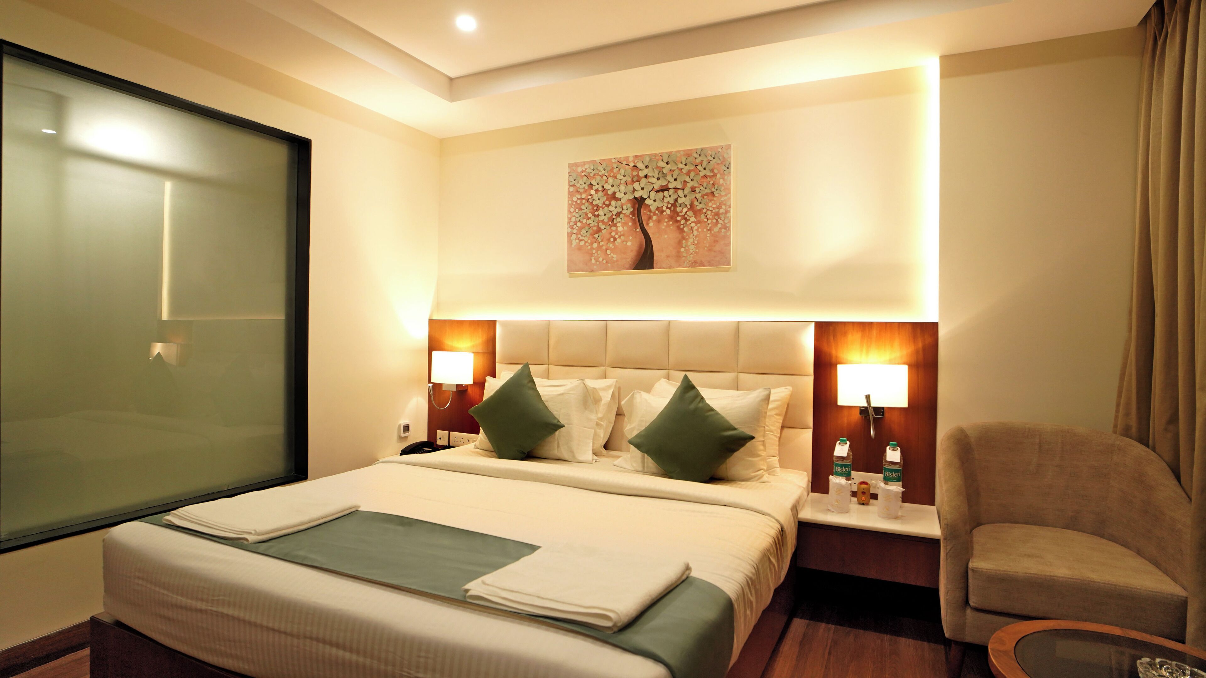 A hotel room with a large bed, two bedside lamps, a nightstand, a chair, and a painting on the wall.