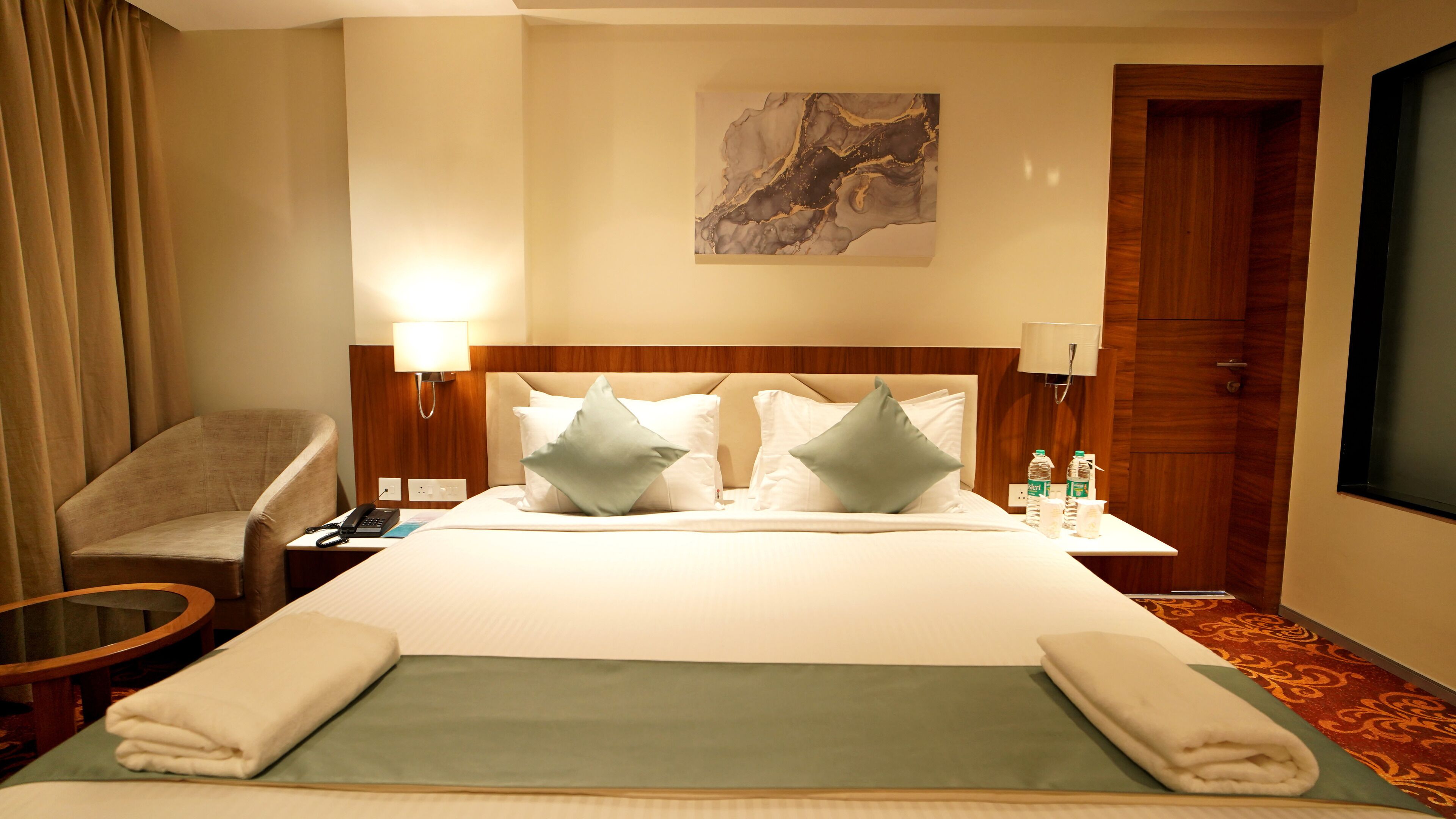 Una habitación de hotel con una cama, una silla, un escritorio con una lámpara y un cuadro en la pared.
