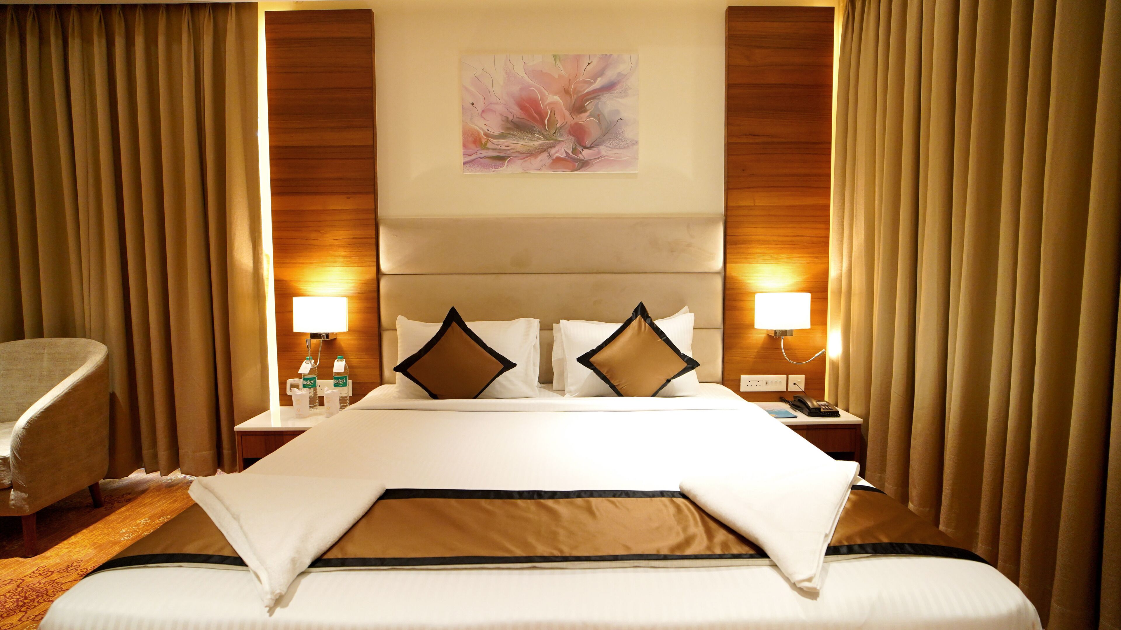 A hotel room with a large bed, two bedside lamps, a headboard, and a painting on the wall.