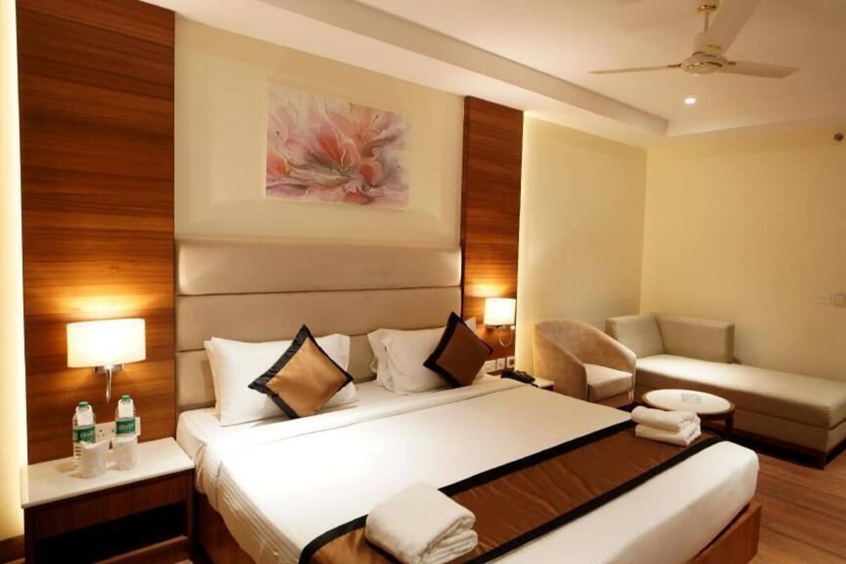 A hotel room with a large bed, a sofa, a chair, a ceiling fan, and a wall-mounted artwork.