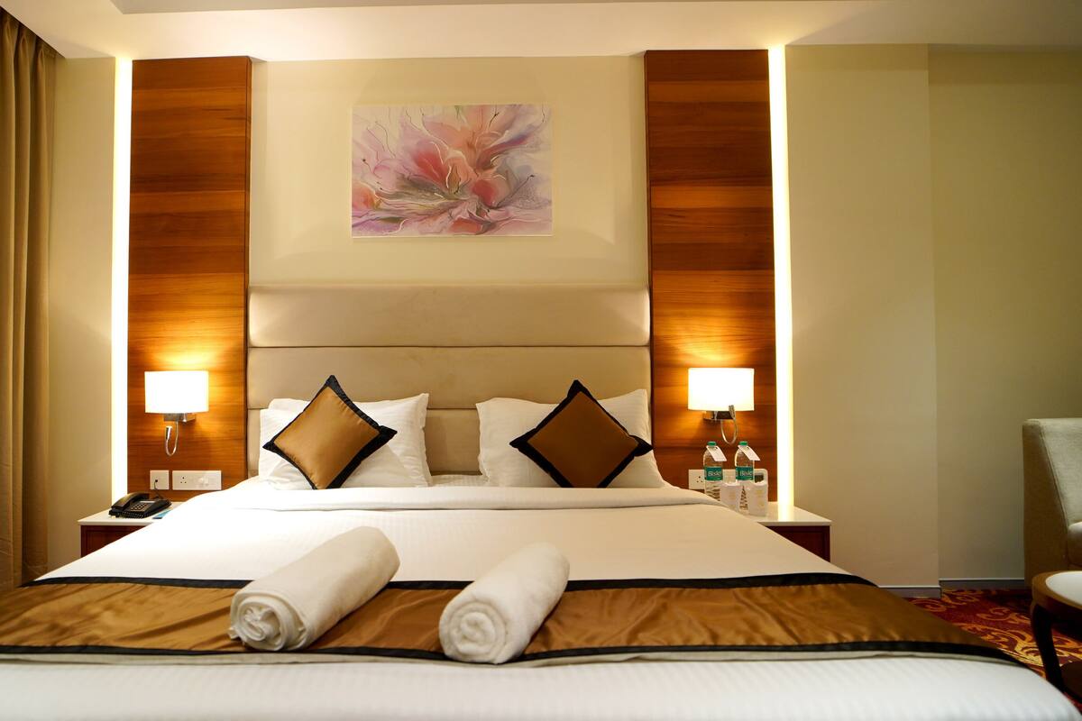 A hotel room with a large bed, two bedside lamps, a painting on the wall, and a chair in the corner.
