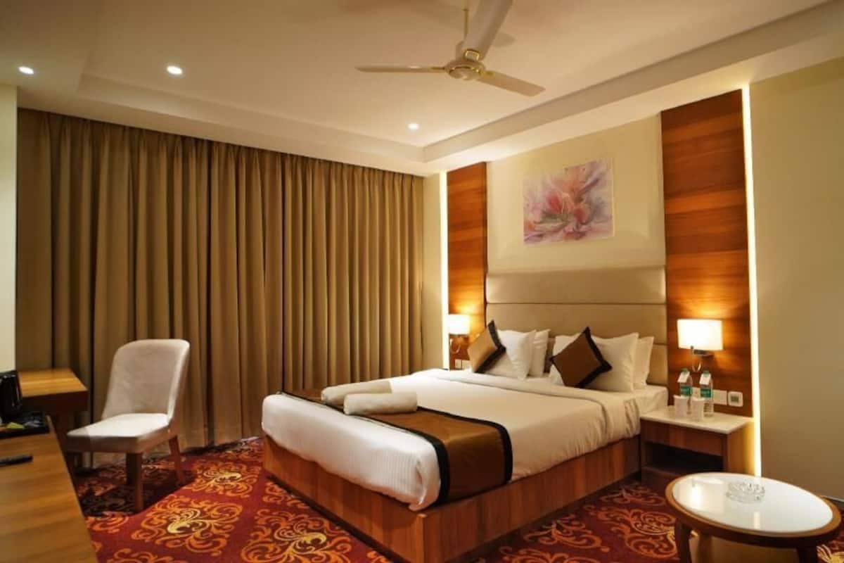 A hotel room with a large bed, a desk, a chair, a round table, and a ceiling fan.