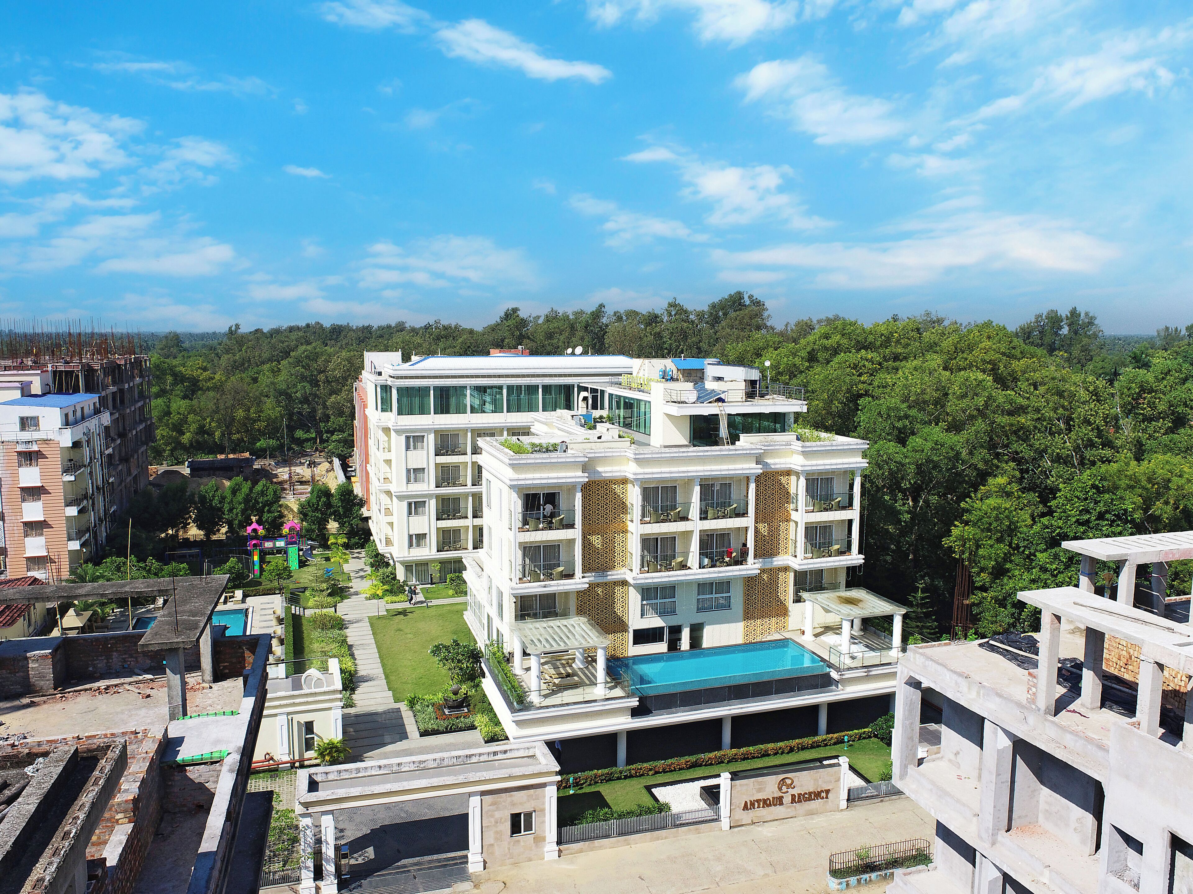 Un hotel de varios pisos con piscina, rodeado de vegetación y otros edificios.