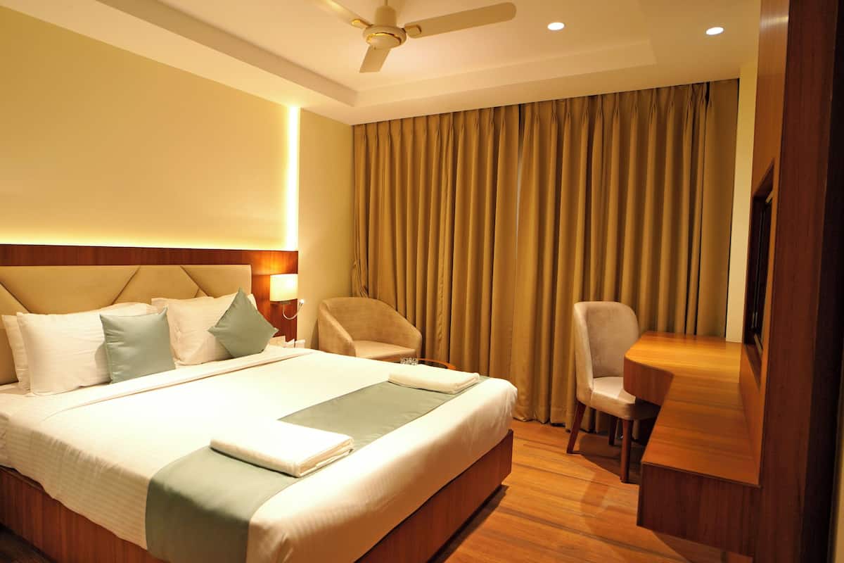 A hotel room with a large bed, a desk, a chair, and a ceiling fan.