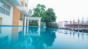 A clear blue swimming pool with a white pergola and a wooden lattice wall.