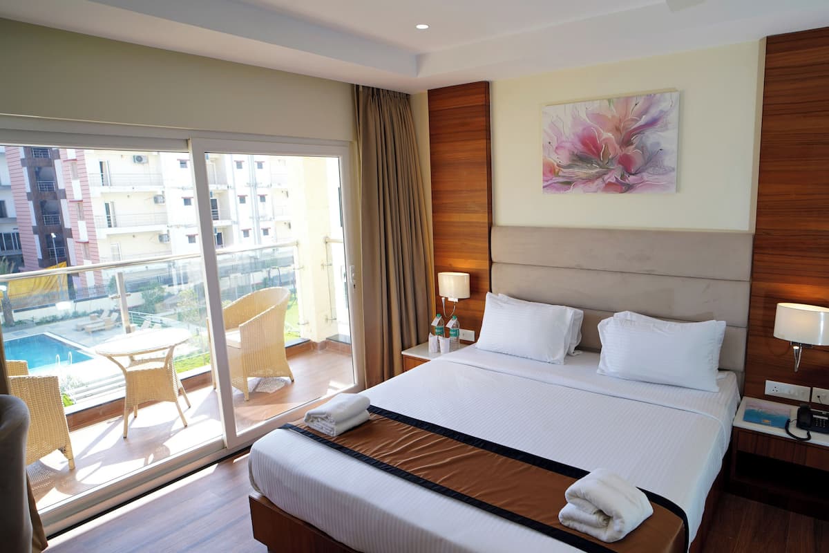 A hotel room with a large bed, two bedside tables, a chair, a balcony with a pool, and a city view.