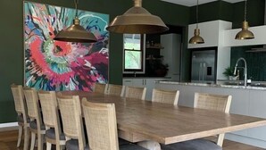 Zona de dinar amb taula i cadires de fusta, un quadre abstracte i lluminàries penjants.
