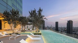 Piscina infinita en la azotea con sillones de descanso, árboles y el horizonte de la ciudad al fondo.