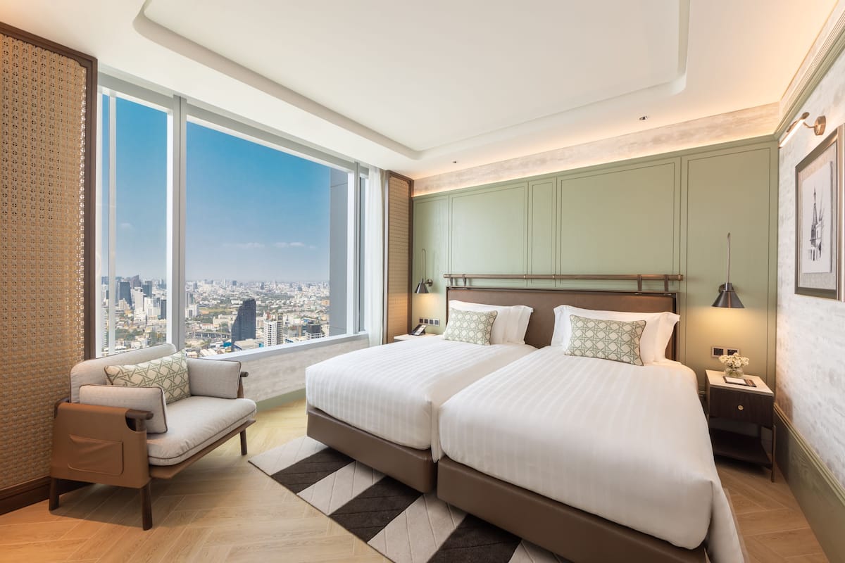 A hotel room with two beds, a sofa, a view of the city, and a large window.