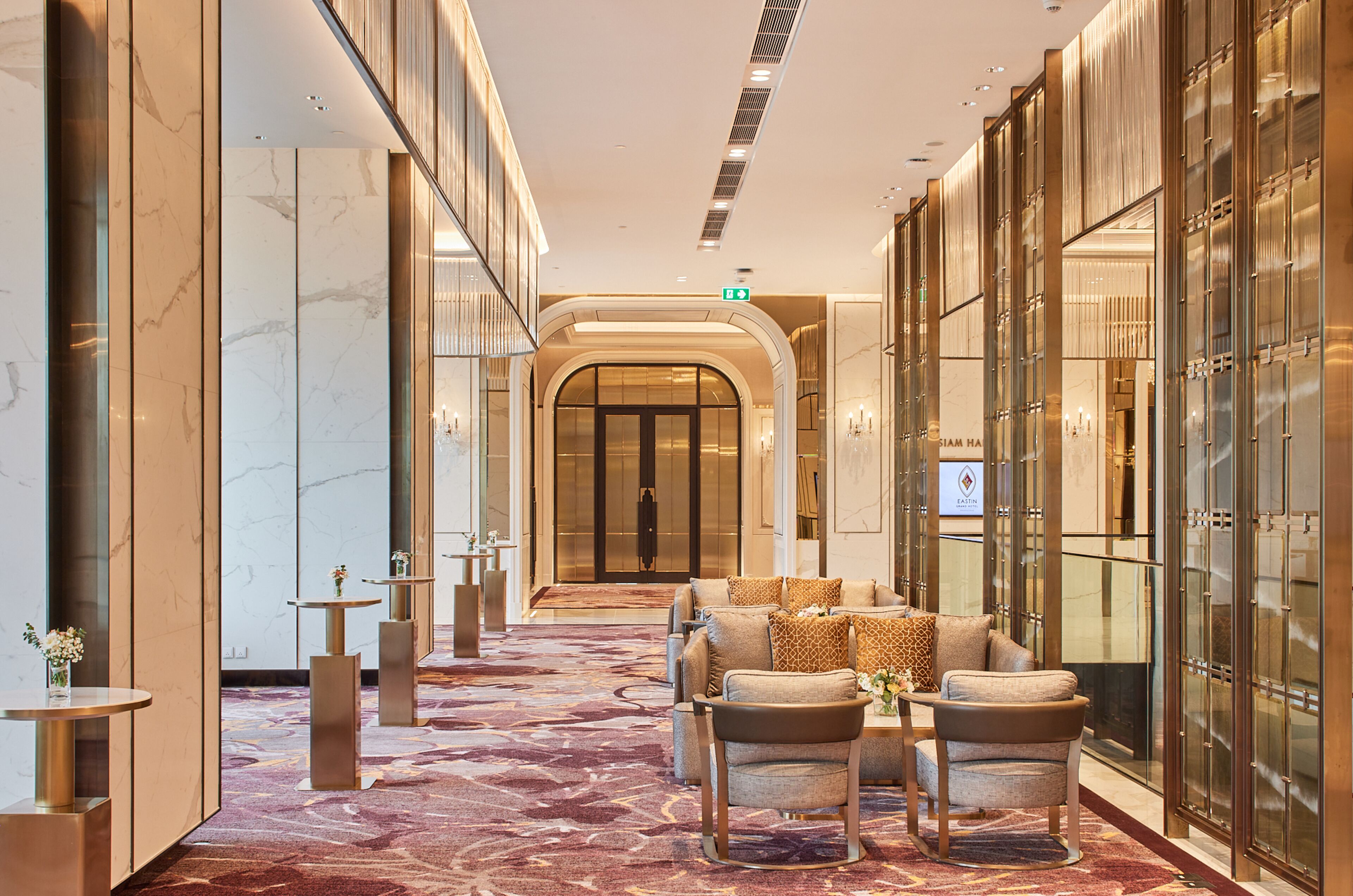 Un hall de hotel con piso de mármol, zona de estar con sofás y sillones, y un separador de vidrio en un lateral.