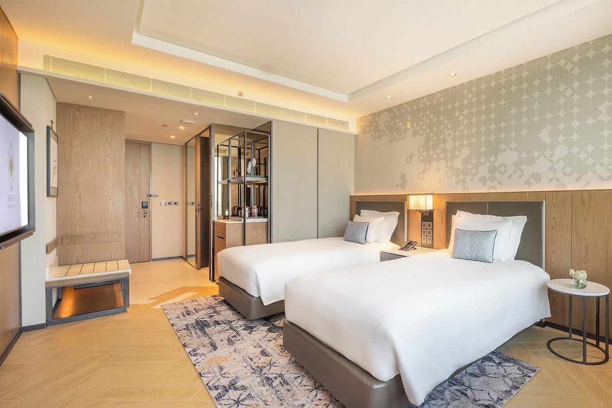 A modern hotel room with two beds, a large mirror, a desk, and a TV.