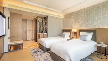 A modern hotel room with two beds, a large mirror, a desk, and a TV.