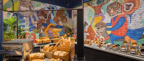 Mostrador de panadería con una variedad de panes y pasteles, una máquina de café y un mural colorido con animales en la pared.