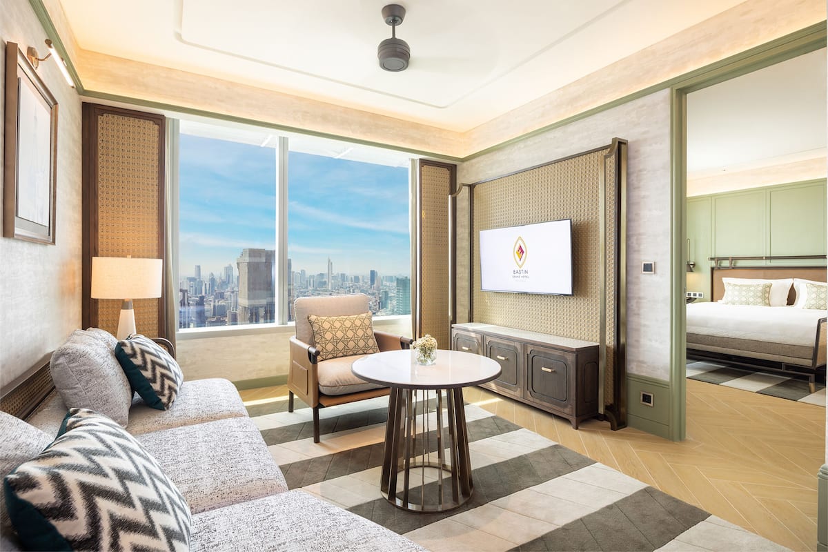 A modern hotel room with a large window, a sofa, a round table, a TV, and a bed.