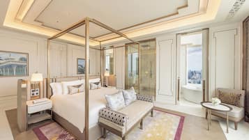 A luxurious bedroom with a four-poster bed, a sitting area with a sofa, a small table, and a view of the city through a glass door.