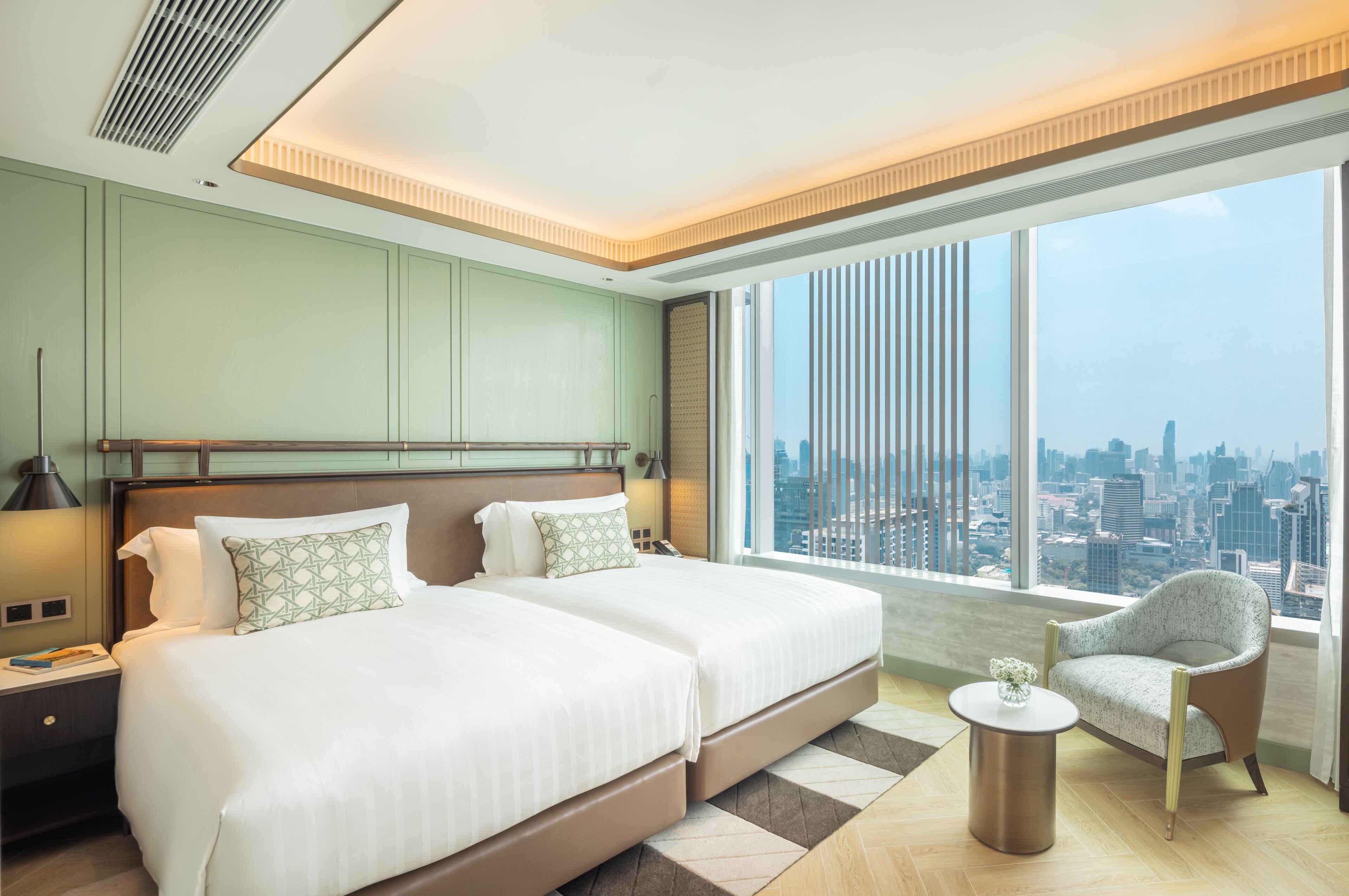 A modern hotel room with two beds, a city view, and a small table with a vase.