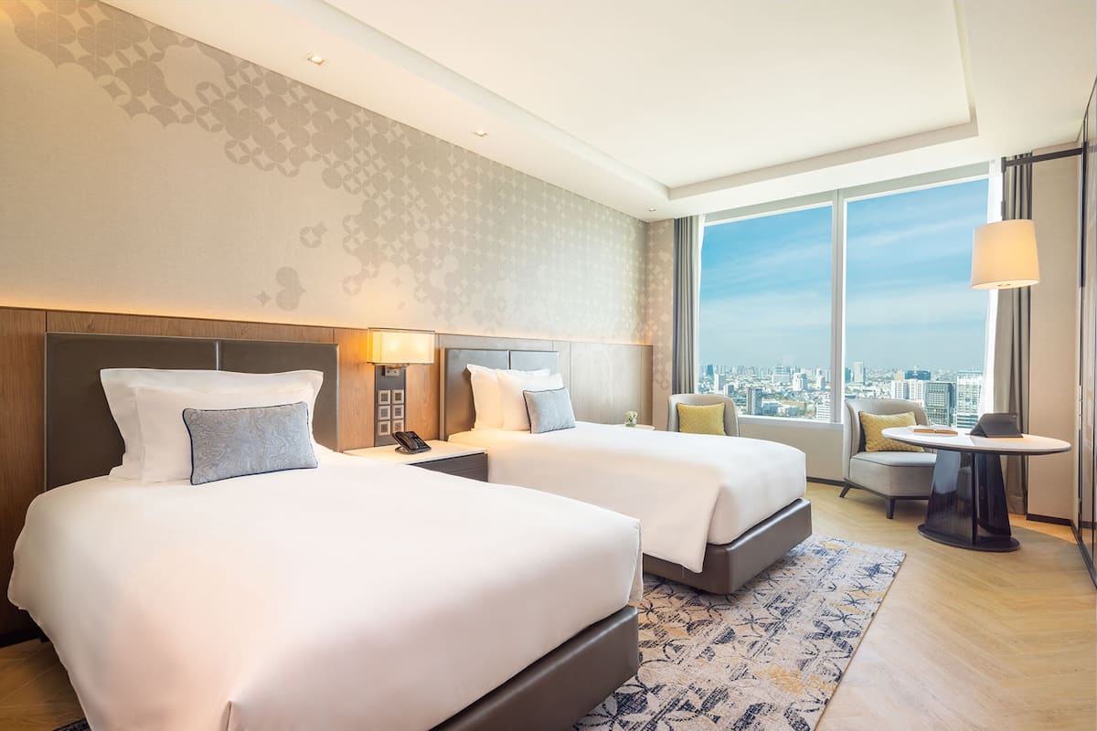 A hotel room with two beds, a city view, a small table, and a chair.