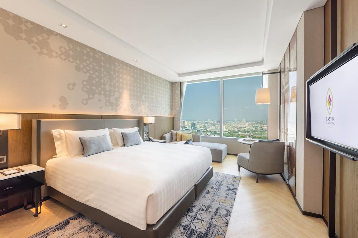 A modern hotel room with a large bed, a desk, a chair, and a TV.