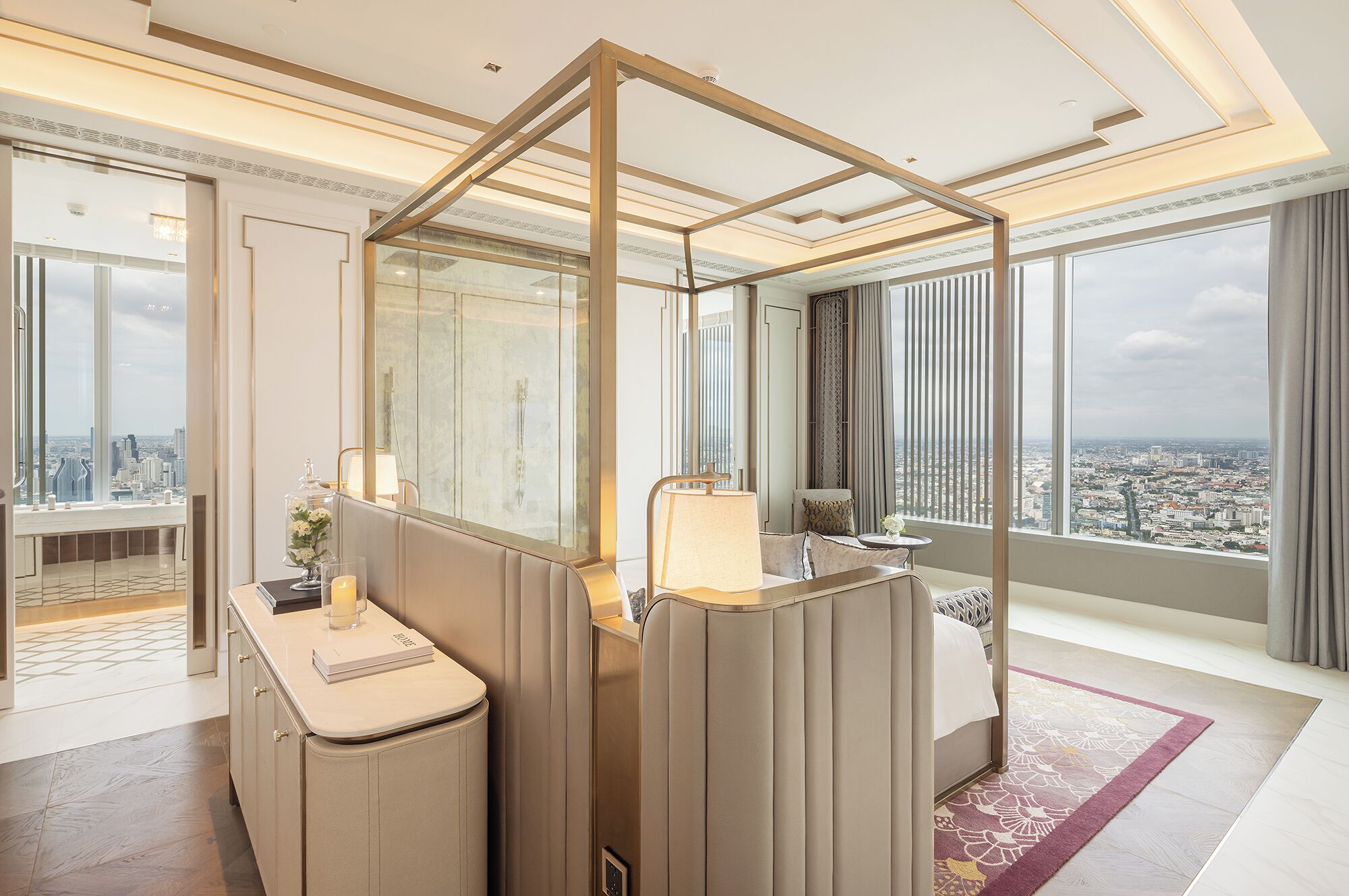 A modern hotel room with a city view, a large mirror, a vanity with a lamp, and a seating area with a view.