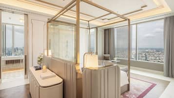 A modern hotel room with a city view, a large mirror, a vanity with a lamp, and a seating area with a view.