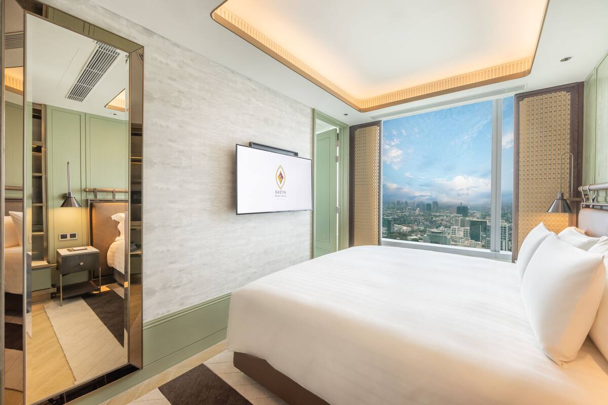 A modern hotel room with a large bed, a city view, a television, and a bathroom with a mirror and sink.