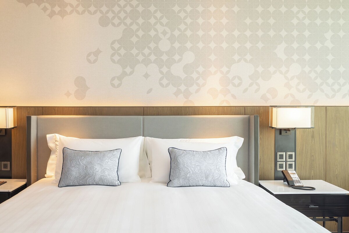 Habitación de hotel con una cama grande, dos lámparas de noche, una mesita de noche con teléfono y una pared con diseño.