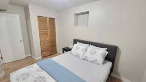 A bedroom with a bed, a nightstand, a wooden wardrobe, and a window.