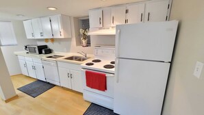 A compact kitchen with white cabinets, a white refrigerator, a stove, a microwave, and a sink.