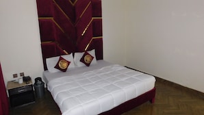 A neatly made bed with a white quilt and two decorative pillows, a red upholstered headboard with gold trim, and a small bedside table with a telephone and a trash bin. - Empire Hotel (Lahore)