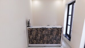A reception desk with a marble top and a white base, situated in a hallway with white walls and a large window on the right. - Empire Hotel (Lahore)