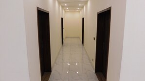 A hallway with white walls, dark wooden doors, and shiny tiled flooring. - Empire Hotel (Lahore)