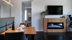 Un comedor moderno con una mesa de madera, cuencos blancos, copas de vino y una botella de vino. Hay un televisor de pantalla plana montado en la pared sobre una chimenea de madera.